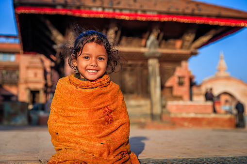 Portrait of Nepali little girl, Gopinath Krishna Temple on the background. Bhaktapur is an ancient town in the Kathmandu Valley and is listed as a World Heritage Site by UNESCO for its rich culture, temples, and wood, metal and stone artwork.