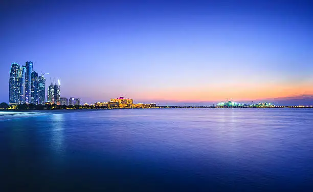 Panoramic view over the Persian Gulf on Abu´s Dhabi´s skyline, with the landmarks Etihad Towers, the Emirates Palace and ongoing offshore constructions on the nearby island at dusk.