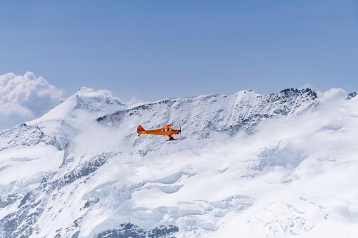 Close up of a small yellow plane flying at 3,700 meters against the backdrop of the Swiss Alps, Valais, Switzerland, with various mountain peaks around the Jungfrau-Aletsch glacier