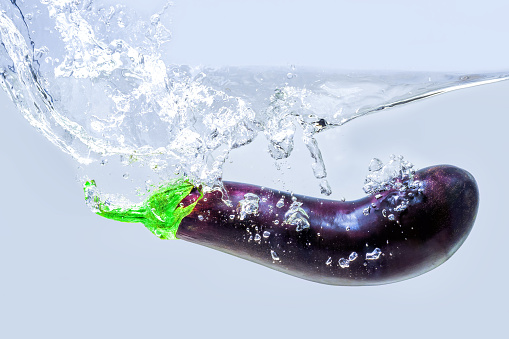 Fresh whole eggplant dropped in water with splashes on gray background