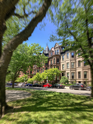 Victorian brownstone townhouses on Commonwealth Avenue border a park in the beautiful and historic Back Bay neighborhood on a warm Spring afternoon.