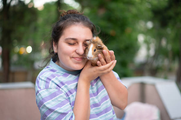 Playing with a brown,hamster,mouse,lemming at home. Holding him in hand and enjoying kissing stroking. Smiling while hamster touches face of a young woman.
