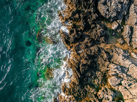 Aerial view of adriatic coastline with waves hitting the rocky beach.