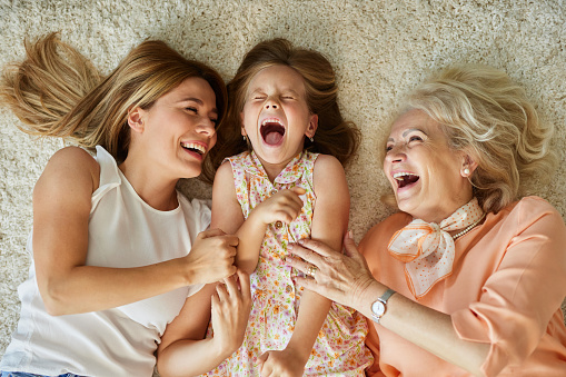 Shot of three generations family relaxing together at home. Cheerful mother and grandmother having fun while playing with their two kids on sofa in the living room.
