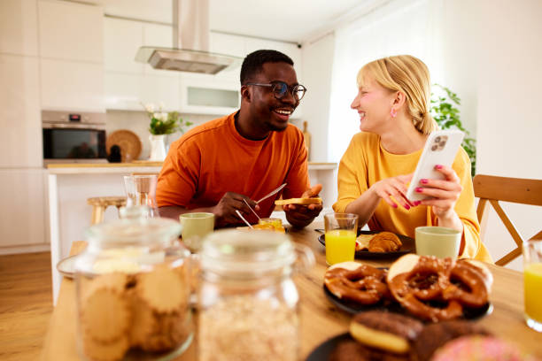 istock Happy multiracial couple using mobile phone together over breakfast at home 1603339888