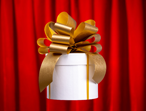 A gift box with gold coloured bow spinning against red curtain