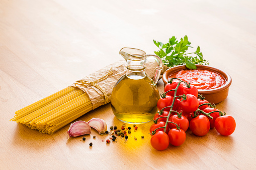 Italian pasta ingredients shot on wooden table. The composition includes raw spaghetti, extra virgin olive oil bottle, tomatoes, salt and pepper, garlic, herbs, among others. High resolution 42Mp studio digital capture taken with SONY A7rII and Zeiss Batis 40mm F2.0 CF lens