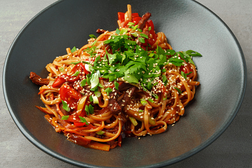 Stir fry noodles with vegetables and beef in black bowl on table close up