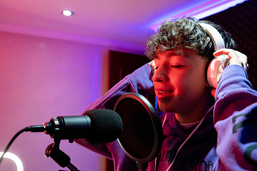 Portrait of a Latin boy singing and having fun on a black background in a music studio, wearing headphones, with a microphone and learning to be a vocalist.