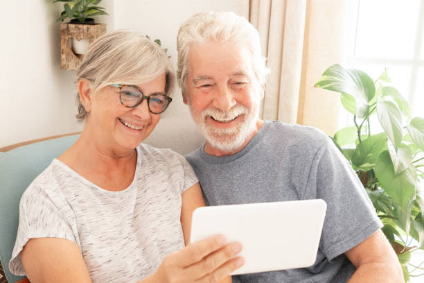istock Video call concept. Smiling senior family couple using digital tablet for online communication via video meeting, smiling white-haired man and woman looking and talking 1603367421