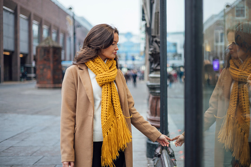 A woman walking down the street of Newcastle-Upon Tyne, she is window shopping. Looking for gifts for her family, friends and relationship. She is wearing a vibrant yellow scarf.