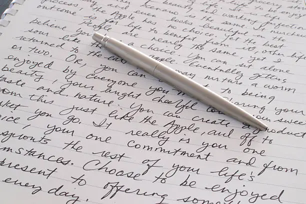 A Stainless Steel Ball Point Pen is Laying on the Written Page of a Spiral Bound Notebook