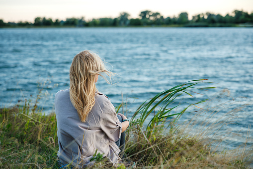 Woman is relaxing in nature by lake to improve her mindfulness and mental health. Enjoyment of fresh air and digital detox outdoors