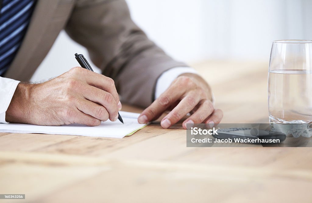 Getting admin out of the way Cropped image of a businessman writing on a piece of paper with his cellphone in front of him Adult Stock Photo