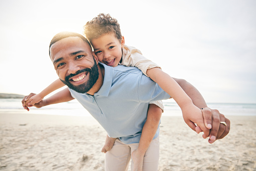 Father, son and piggyback, beach and portrait with love and bonding, travel and ocean with holiday, fun and happiness. Playful, smile and trust, man and boy together with vacation and sea adventure