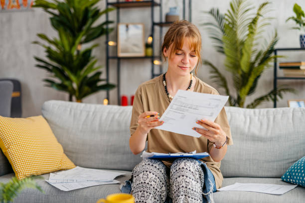 Young Woman Checking Her Finances At Home Young woman checking her finances while sitting on the sofa at home. savings account stock pictures, royalty-free photos & images