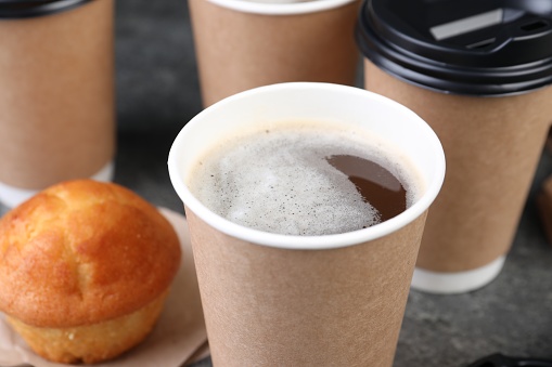 Coffee to go. Paper cups with tasty drink and muffin on table, closeup