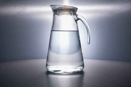A glass decanter filled with clean drinking water beautifully illuminated on a gray background. Water advertising. Jug. Water is life. Space for text. CopySpace. no people. subject shooting.