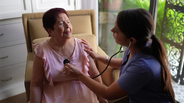 Home caregiver listening to a senior woman's heartbeat in a nursing home