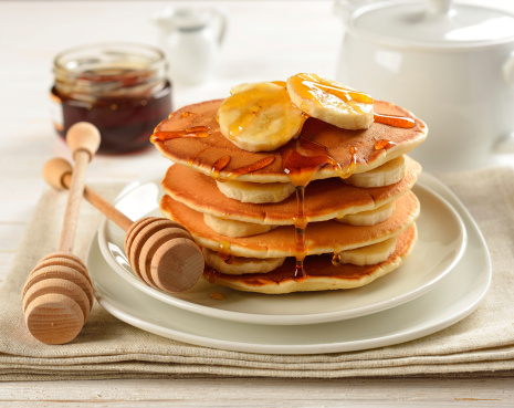 Pancakes with banana and honey on a white table