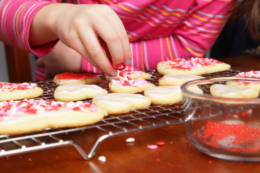 A young girl adds heart sprinkles to her Valentine's cookies.  Don't they look delicious?