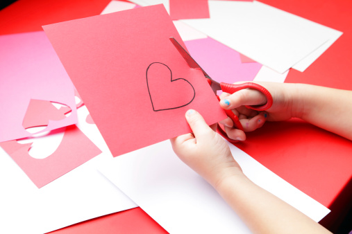 A young girl cuts out a paper heart to use for her Valentine's Day card.  