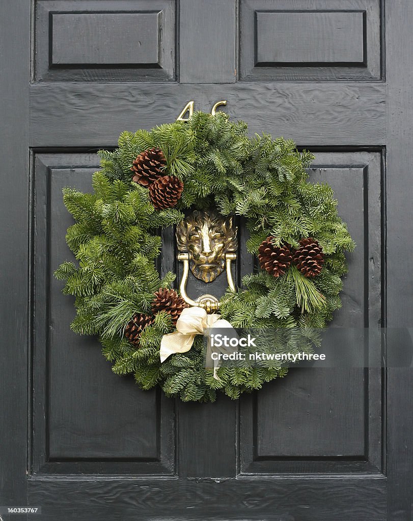 Fresh Christmas wreath on a door Fresh Christmas holiday wreath on an old style English black wooden door with a gold lion head knocker Wreath Stock Photo