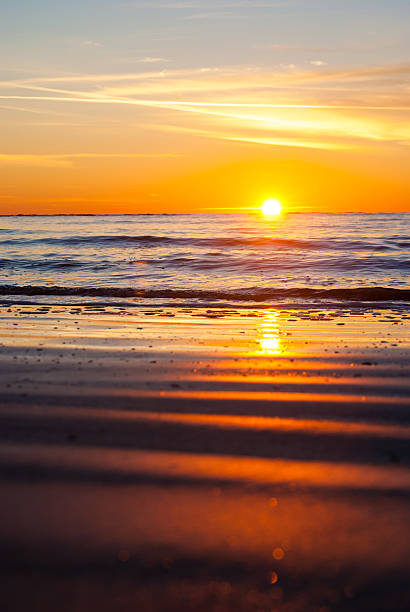 Golden sunrise reflection on beach sand stock photo
