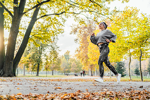 Young cheerful sporty woman running in the autumn park