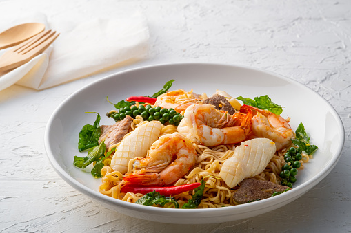 Spicy Stir Fried Instant Noodle with Seafood and basil in white plate