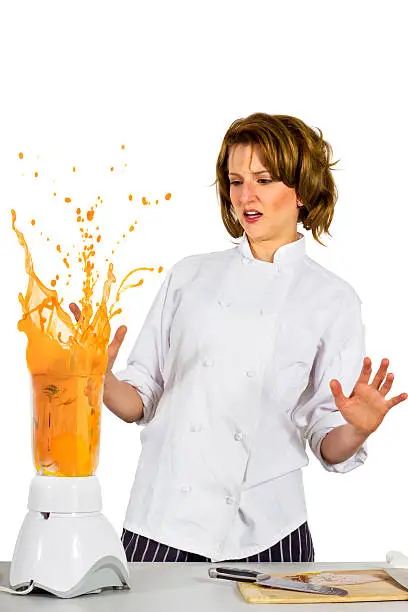 young Cacucasian female chef forgot to put the lid on the blender and is making a mess. isolated on a white backgorund.