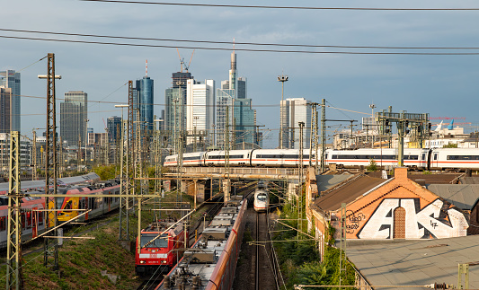 Train and skyline Frankfurt Germany - July 19, 2023: ICE and cargo train leaves Frankfurt. Signaling systems, railroad ties and switches. Buildings, skyscrapers in the background.