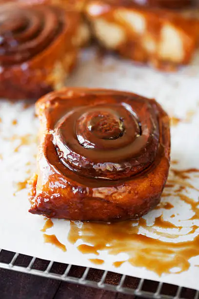 Freshly-baked sticky buns glazed with caramel sauce, cooling on a rack.