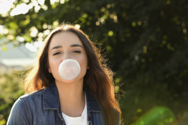 istock Beautiful young woman blowing bubble gum in park. Space for text 1603589331
