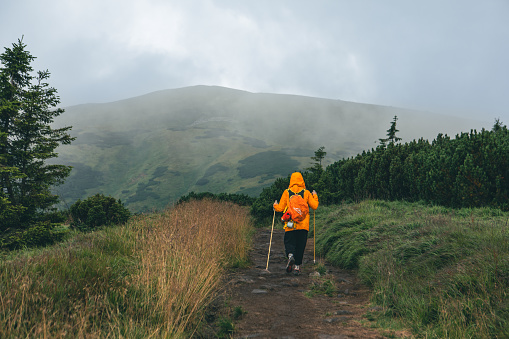 woman in yellow raincoat at mountain trail road copy space hiking concept