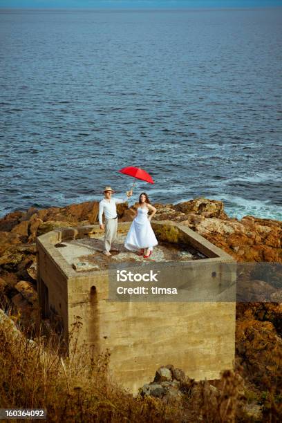 Bride And Groom On Concrete Bunker With Red Umbrella Stock Photo - Download Image Now