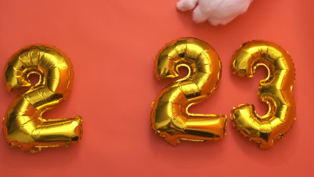 flat lay inflatable golden balloons in the form of numbers 2023 on orange background. Year of the rabbit. White rabbit instead of zero. Happy New Year. greeting card