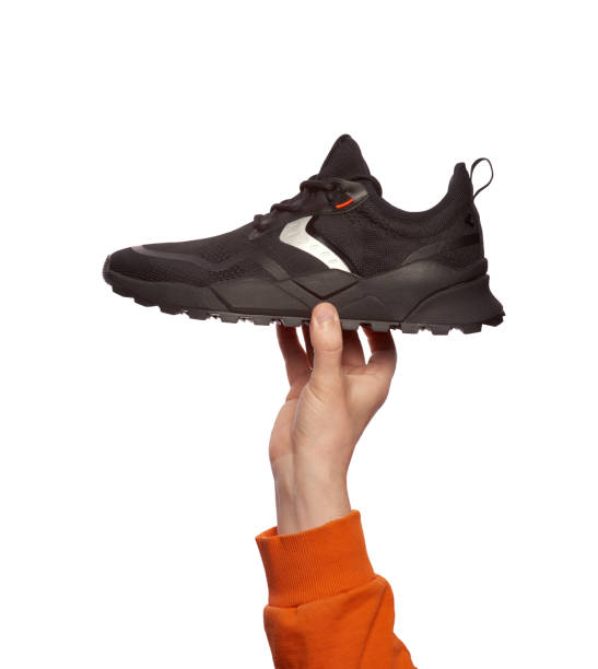 istock A man's hand holding a trendy black sneaker isolated on a white background. Creative minimalistic layout with sports footwear. Discount promotion poster 1603684003