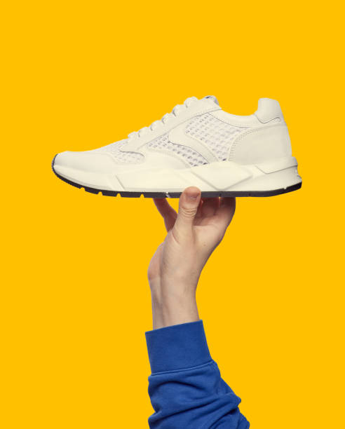 istock Hand holds white running sneaker on bright yellow background with copy space. Close up. Outlet marketing poster 1603684024