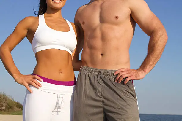 close up waist shot of fit couple in sports wear with perfect bodies on the beach