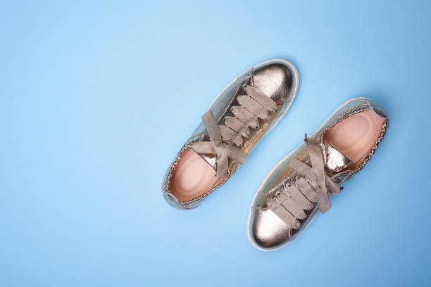 istock Shiny sneakers in metallic gold leather on a gradient blue background. Top view, flat lay. Creative minimalistic layout with shoes 1603690990