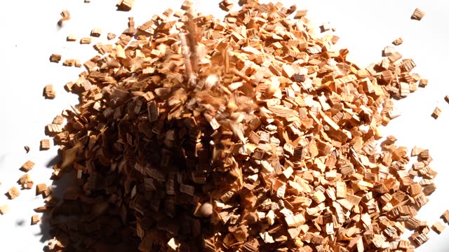 Wood chips fall from above on a white table, a large pile of wooden chips is already on the table
