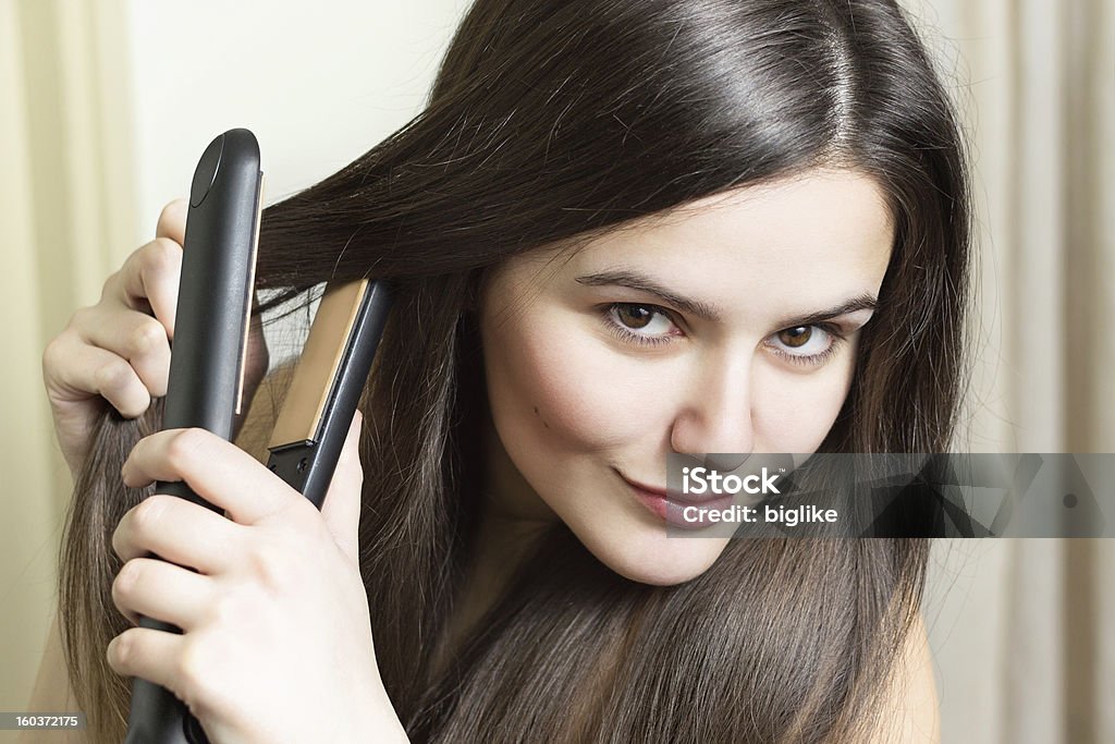 Young sultry woman straightening her hair Headshot of a beautiful young woman straightening hair and looking at camera smiling Domestic Bathroom Stock Photo