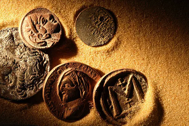 Few ancient coins on sand background under beam of light