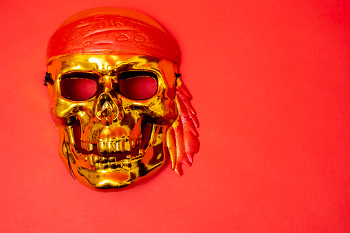 a golden skull with a red headband on a red background. Halloween, piracy. Jolly Roger. The sign of the pirates. Crimes of robbery, Sea robbers. Banner. Space for text. Copy space.