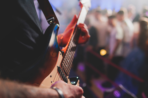 Concert view of an electric guitar player with vocalist and rock band performing in club, male musician guitarist on stage with audience in a crowded concert hall arena