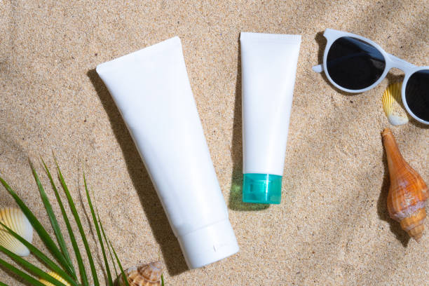 istock Sunscreen container mockup with sea shells, sunglasses, and palm leaf on sand background 1603743526