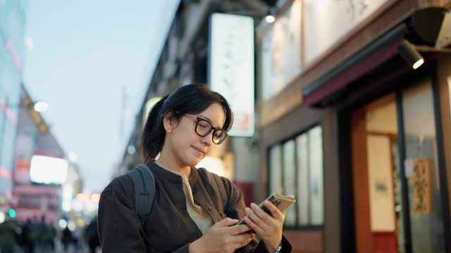 Happy Asian woman with a smile walks on the streets of Japan and uses a smartphone to take pictures during her vacation.