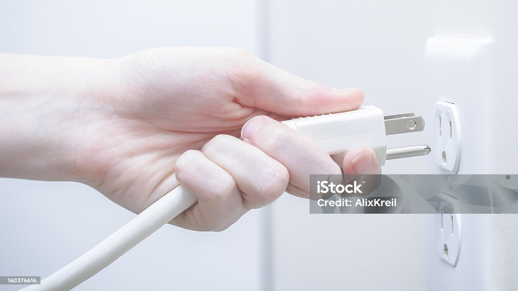 Plugging in a power cord A woman plugging in a power cord to a wall outlet. Plugging In Stock Photo