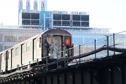 New York, NY USA - January 16, 2023 : Front car of a northbound New York City MTA 1 train coming down the elevated subway tracks in Manhattanville, Harlem, with Columbia University's Jerome L. Greene Science Center in the background